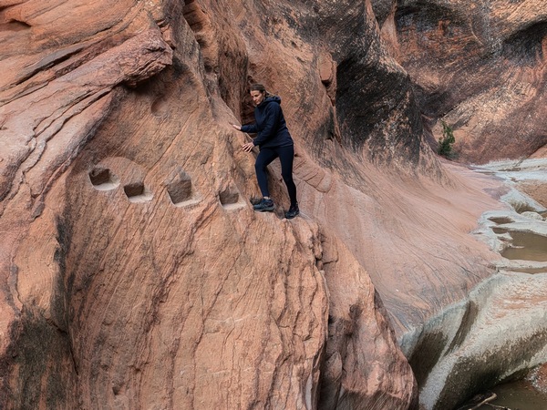woman hiking the red reef trail in the Red Cliffs National Conservation Area in Utah. she is utilizing steps that have been carved into the side of a slot canyon wall