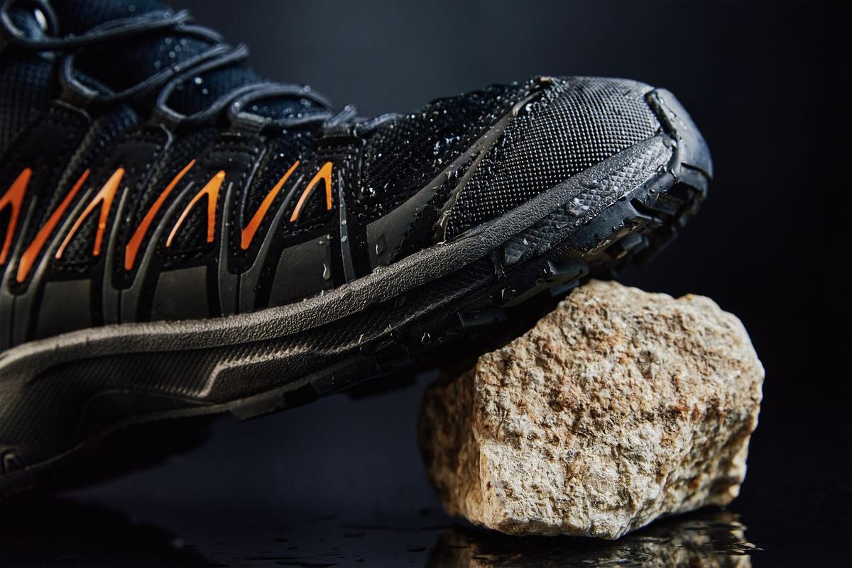 Close-up of a lugged hiking boot on wet rock beside a stone